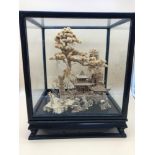 A Large Chinese cork carving of landscape scene with pagoda, in a glass case on a carved stand.