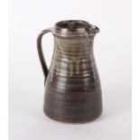 A stoneware jug in the style of Bernard Leach of ribbed tapering form with an impressed mark (H: