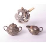 A Japanese matched three piece white metal teaset, each part decorated with embossed flaming