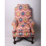 An upholstered wing armchair, probably French with a shaped back scrolled arm supports with X