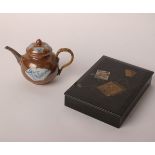 A small globular Chinese tea pot with two fan panels on a brown ground with cane handle, white metal