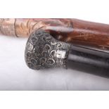 A walking stick, topped with embossed white metal, marked indistinctly, and a metal ferrule.