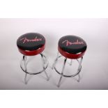 A pair of bar stools with chrome supports, metallic red and black seats with 'fender' logo