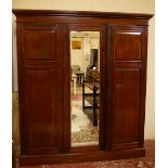 A late Victorian mahogany triple wardrobe, outswept cornice, central mirrored door flanked by