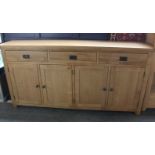 A solid light oak sideboard with three drawers and four cupboards. H: 100cm w: 200cm d: 45cm