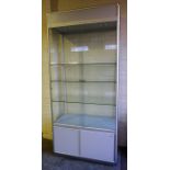 A Large Shop Cabinet, with sliding glazed doors, enclosing three glass shelves and spotlights to the