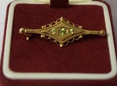A 9ct Gold and Peridot Brooch, With a central peridot stone, flanked with a smaller stone, stamped