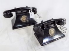 A pair of child's black bakelite battery operated telephones linked by twisted wire cord,