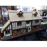 A dolls house in the style of a period country cottage with thatched roof with ten rooms and fully