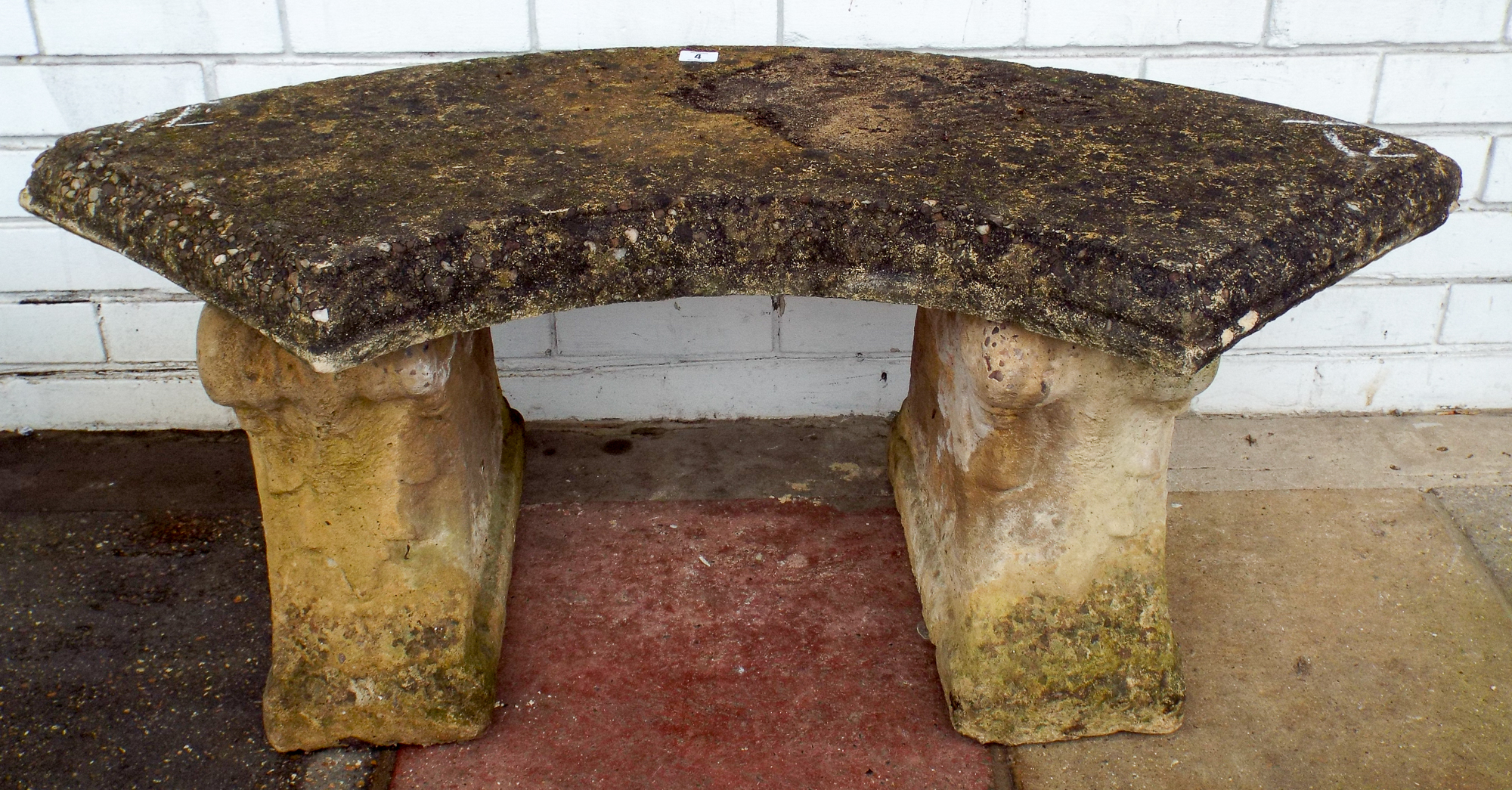 An arc shaped reconstituted stone garden bench on concrete base