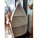 A pink and white painted boat shaped book shelf with oars