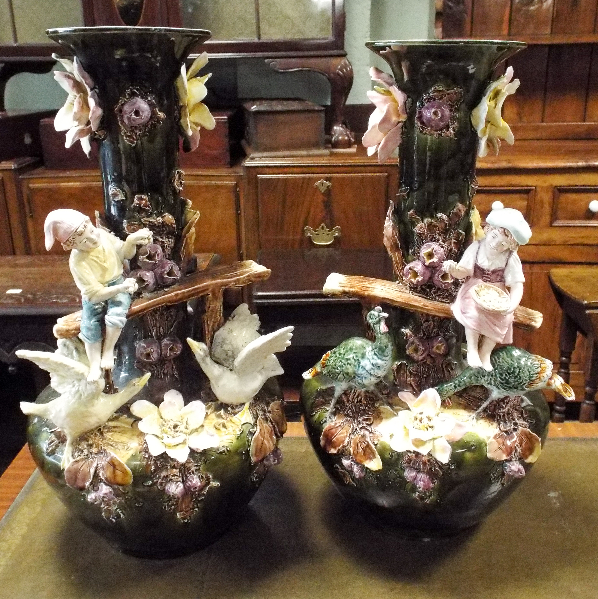 A pair of large china vases decorated with flowers and a young boy and girl on benches feeding the