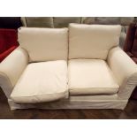 A modern two seater settee in cream covering with loose cushions