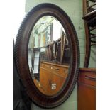 Two early 20th century oval bevelled wall mirrors in wood effect frames