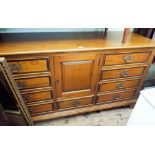 A heavy oak finished sideboard with centre cupboard and nine mahogany cross banded drawers with