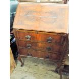 A figured walnut bureau with three drawers under standing on cabriole legs.