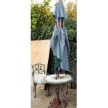 A circular tile top patio table with two green painted elbow chairs with cushions and a parasol