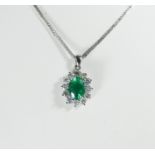 An 18ct white gold emerald and diamond cluster pendent set with a central oval cut emerald