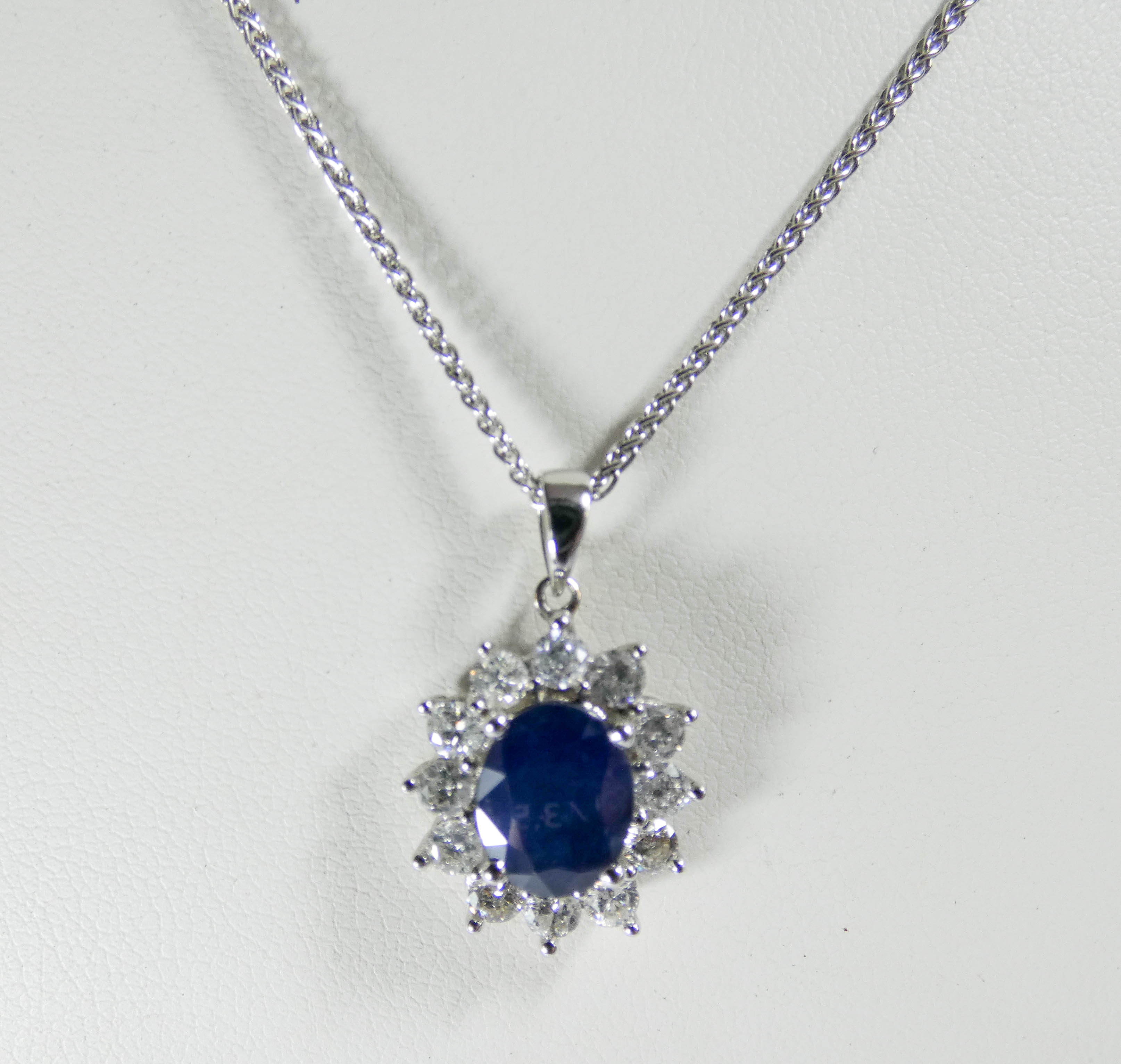 An 18ct white gold sapphire and diamond cluster pendent set with an oval sapphire surrounded by 12