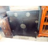 A Chinese style black lacquered two door cupboard fitted with a drawer,