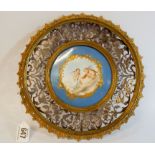 A continental porcelain enamel plaque depicting cherubs feeding swans in a silver gilt decorative