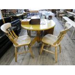 A circular light pine single pillar breakfast table and a pair of Windsor farmhouse style kitchen