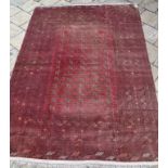 An Afghan carpet, with repeating geometric shapes on a red ground,
