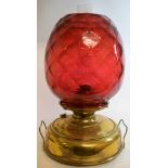 A large oil lamp, with a quilted cranberry glass shade on a brass reservoir,