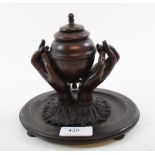 A bronze inkwell, in the form of an urn being held aloft by two hands, on an oval base,