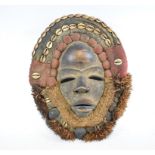 An African native carved wood face mask, within a rope and fabric surround decorated shells,