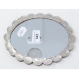 An Indian silver coloured metal mounted mirror, of shaped oval form, embossed flowers and foliage,