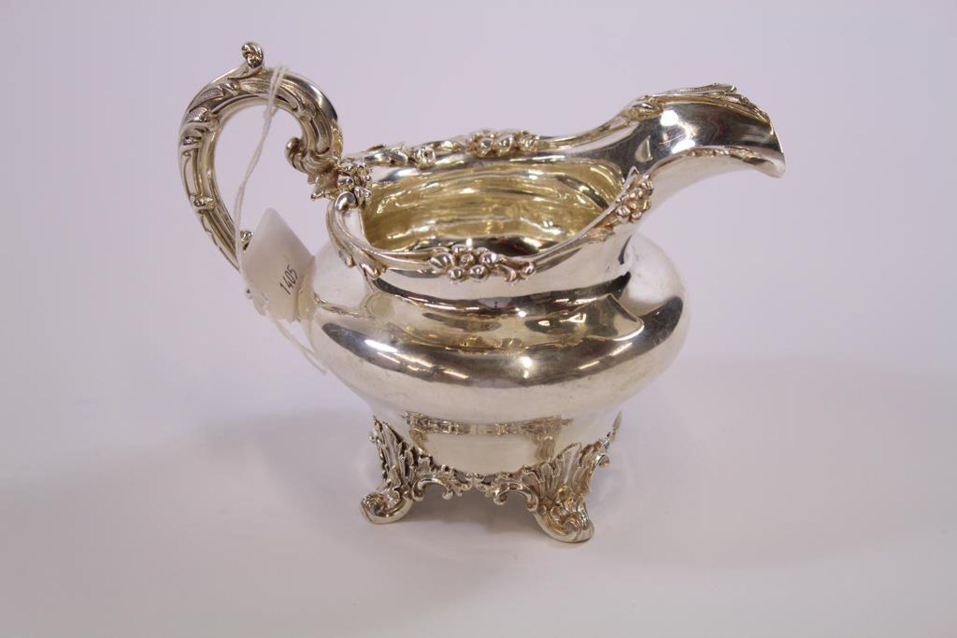 A William IV silver Cream Jug of bulbous form with scroll handle, ornate rim and curving supports (