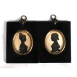 A pair of black framed silhouettes of young ladies, with gold highlights, the frames with acorn