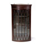 A mahogany bowfronted wall mounted corner cupboard, the astragal glazed door enclosing a shelved