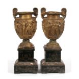 A pair of Victorian two-handled bronze urns mounted on a black slate plinth, decorated in relief