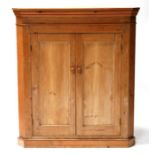 A large Victorian stripped pine corner cupboard, the pair of cupboard doors enclosing shaped