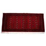 A Turkoman woollen hand made rug with repeat geometric design on a red ground, 140 by 65cms (55 by