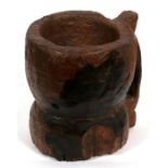 An early wooden mortar of waisted form, with single handle, 19cms (7.5ins) high.