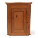 A pine corner cupboard, the single door enclosing a shelved interior, 62cms (24.5ins) wide.
