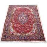 A Heriz woollen handmade carpet with stylised central medallion within a geometric border, on red