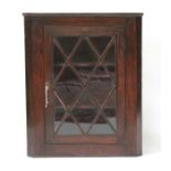 A 19th century oak corner cupboard with glazed door enclosing shaped shelved interior, 71cms (28ins)