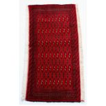 A Turkoman woollen hand made rug with repeat geometric design on a red ground, 110 by 55cms (43 by