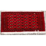 A Turkoman woollen hand-made rug with geometric designs on a red ground, 110 by 50cms (43 by 19.