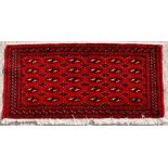 A Turkoman woollen hand-made rug with geometric designs on a red ground, 130 by 65cms (51 by 25.