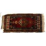 A small Caucasian rug with central gul within a geometric border, on a red ground, 52 by 100cms (