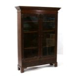 An oak glazed bookcase, carved with foliate scrolls and green man masks, the pair of glazed doors