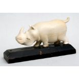 An early 20th century South Sudan carved ivory figure of a rhinoceros, mounted on a hardwood plinth,