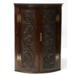 An early 19th century bow fronted oak wall corner cabinet, the pair of carved doors decorated with