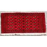 A Turkoman woollen hand-made rug with geometric designs on a red ground, 110 by 50cms (43 by 19.