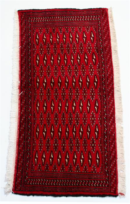 A Turkoman woollen hand made rug with repeat geometric design on a red ground, 110 by 55cms (43 by